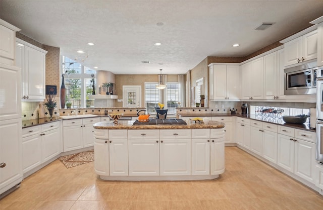 kitchen with kitchen peninsula, white cabinets, stainless steel microwave, a textured ceiling, and pendant lighting