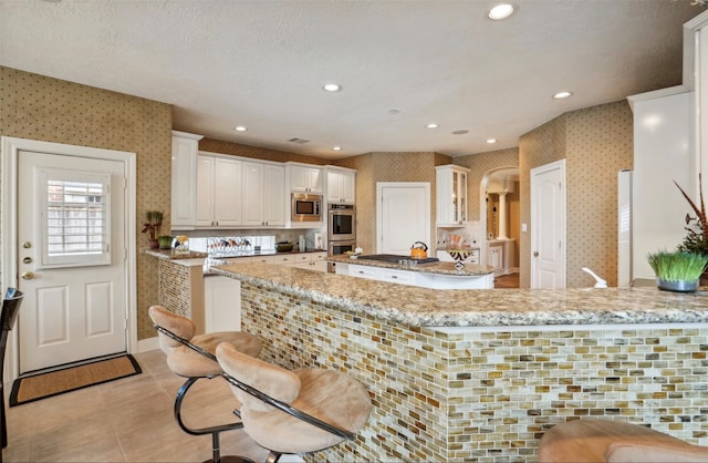 kitchen with white cabinetry, light stone counters, stainless steel appliances, and kitchen peninsula