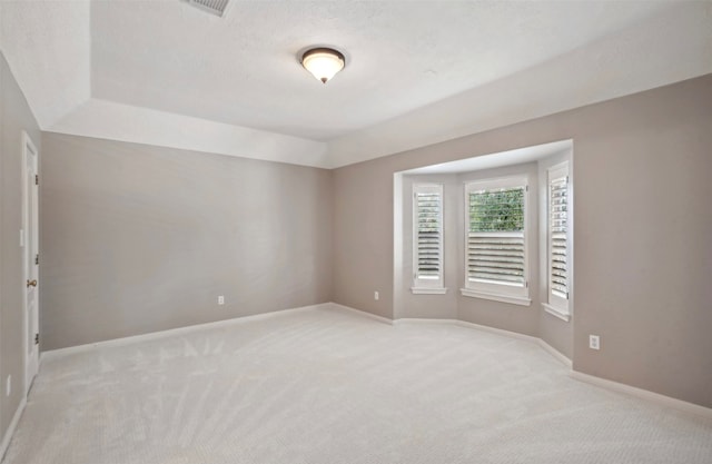 unfurnished room featuring light carpet, a textured ceiling, and a raised ceiling