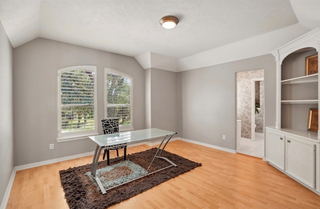 home office with lofted ceiling, built in shelves, a textured ceiling, and light wood-type flooring