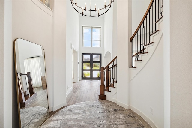 foyer entrance featuring french doors, hardwood / wood-style floors, an inviting chandelier, and a towering ceiling