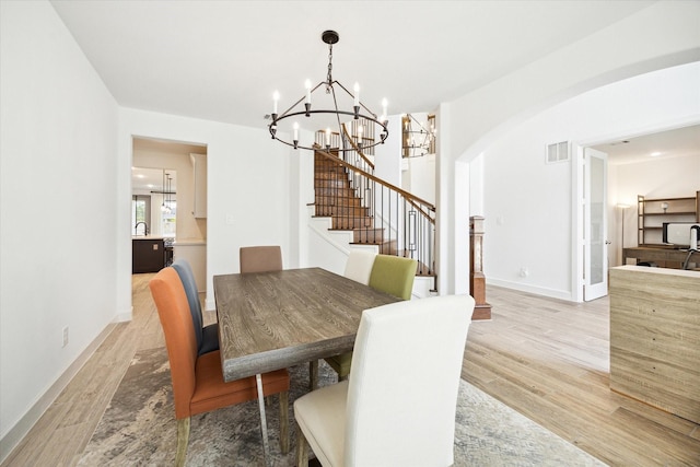 dining area with sink, light wood-type flooring, and an inviting chandelier