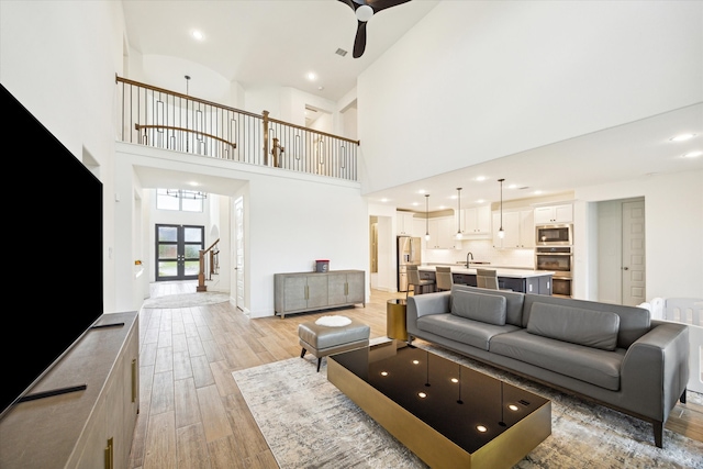 living room featuring a towering ceiling, ceiling fan, light hardwood / wood-style flooring, and sink