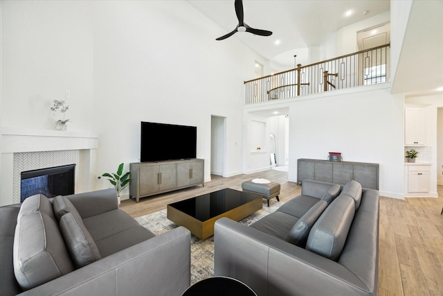 living room with a high ceiling, a tiled fireplace, ceiling fan, and light hardwood / wood-style flooring