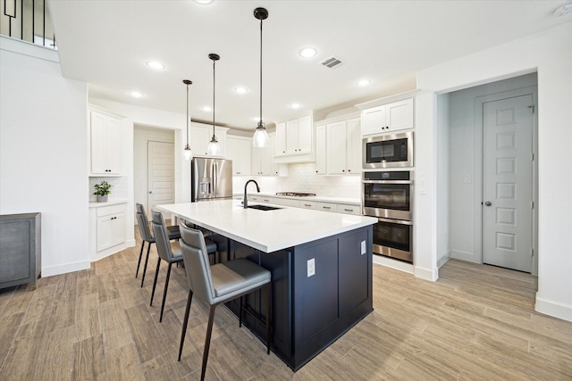 kitchen featuring pendant lighting, sink, white cabinets, stainless steel appliances, and a center island with sink