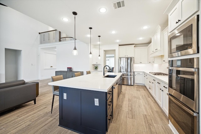 kitchen with sink, white cabinets, decorative light fixtures, a kitchen breakfast bar, and a kitchen island with sink