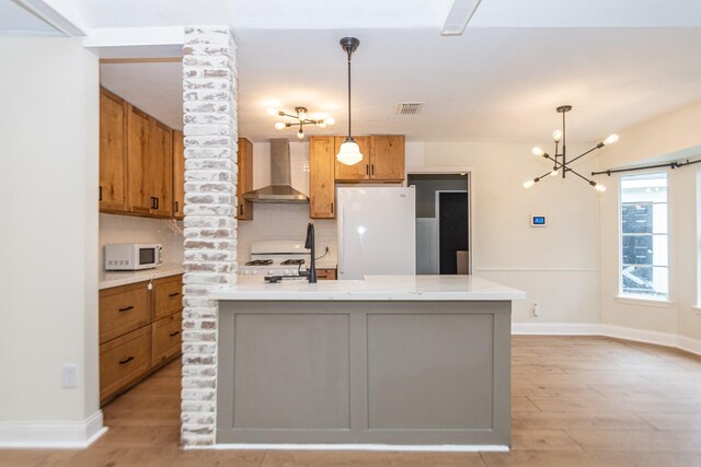 kitchen featuring white appliances, backsplash, hanging light fixtures, wall chimney exhaust hood, and a center island with sink