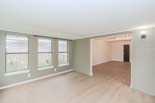 empty room featuring brick wall, light hardwood / wood-style flooring, and a healthy amount of sunlight