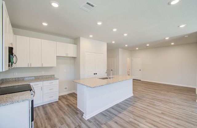 kitchen featuring stove, sink, a kitchen island with sink, white cabinetry, and light wood-type flooring