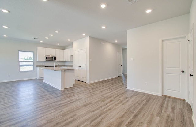 kitchen featuring a center island with sink, light stone countertops, light hardwood / wood-style floors, and white cabinets