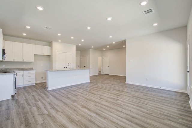 kitchen with light hardwood / wood-style flooring, a kitchen island with sink, light stone countertops, and white cabinetry