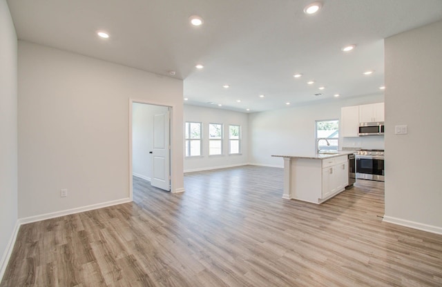 kitchen with sink, a kitchen island, white cabinetry, appliances with stainless steel finishes, and light hardwood / wood-style floors