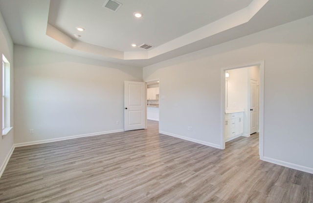 empty room with a raised ceiling and light wood-type flooring