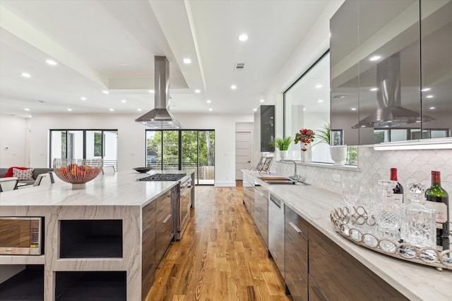 kitchen with light hardwood / wood-style flooring, backsplash, light stone counters, stainless steel appliances, and island range hood