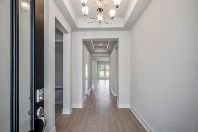 corridor featuring a chandelier, a tray ceiling, and hardwood / wood-style flooring