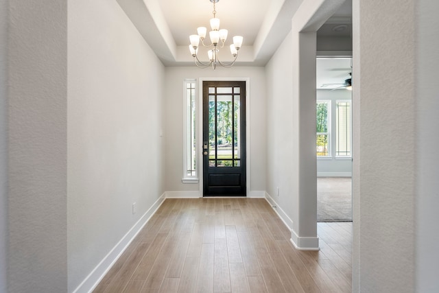 foyer featuring ceiling fan with notable chandelier, a raised ceiling, and light hardwood / wood-style floors