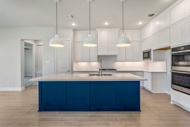 kitchen featuring tasteful backsplash, stainless steel double oven, a center island with sink, black microwave, and light hardwood / wood-style flooring