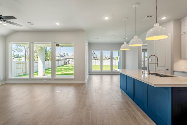 kitchen with light wood-type flooring, ceiling fan, sink, pendant lighting, and a center island with sink