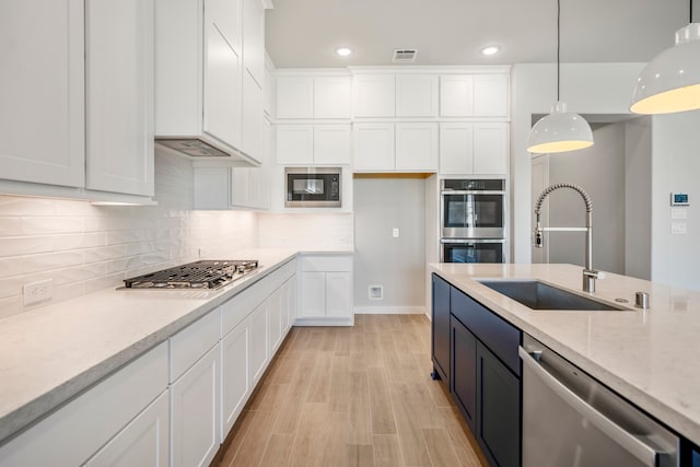 kitchen featuring tasteful backsplash, stainless steel appliances, hanging light fixtures, sink, and light stone counters