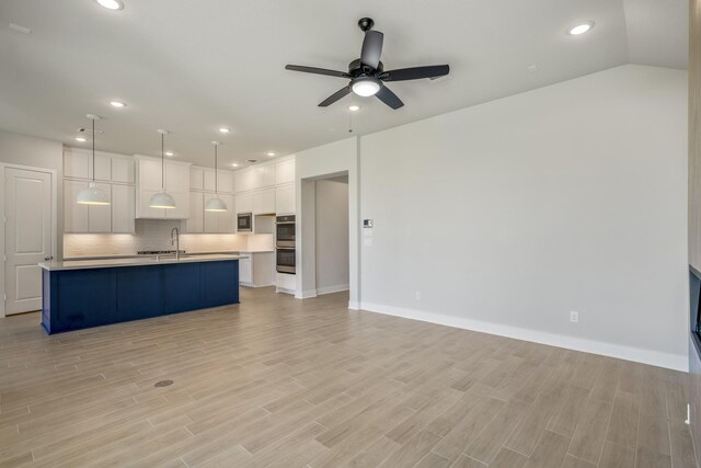 kitchen featuring a center island with sink, hanging light fixtures, backsplash, white cabinetry, and ceiling fan