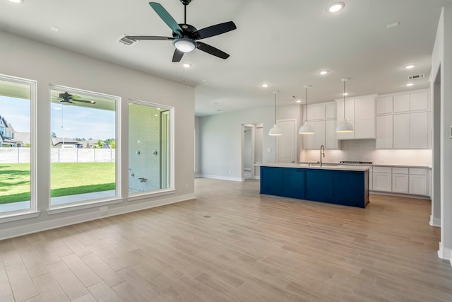 kitchen featuring white cabinets, sink, decorative backsplash, a kitchen island with sink, and ceiling fan