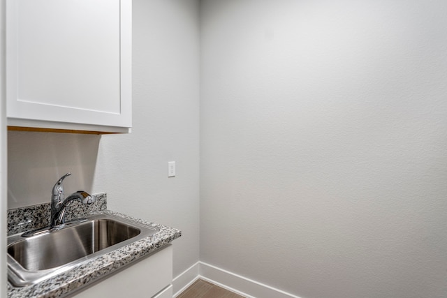 kitchen with sink, light stone countertops, hardwood / wood-style flooring, and white cabinets