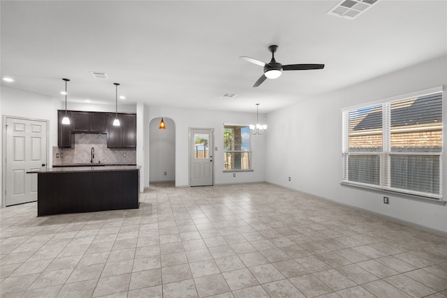 kitchen with light tile patterned flooring, ceiling fan with notable chandelier, decorative backsplash, dark brown cabinetry, and sink