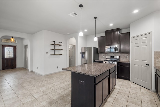 kitchen with dark brown cabinetry, arched walkways, dark stone countertops, a center island, and stainless steel appliances