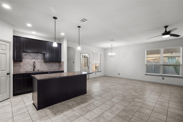 kitchen featuring light tile patterned flooring, tasteful backsplash, hanging light fixtures, ceiling fan with notable chandelier, and sink