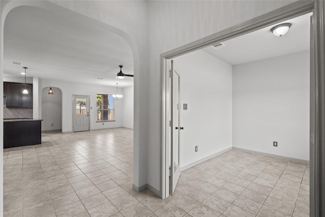 empty room with arched walkways, light tile patterned floors, visible vents, baseboards, and ceiling fan with notable chandelier