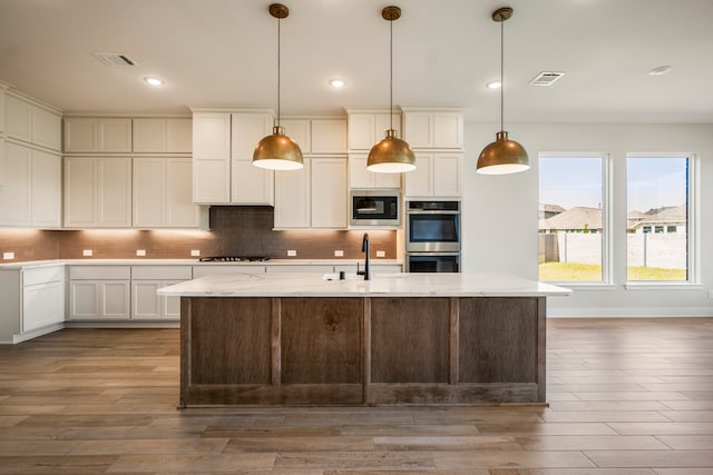 kitchen featuring tasteful backsplash, gas stovetop, black microwave, stainless steel double oven, and hardwood / wood-style flooring