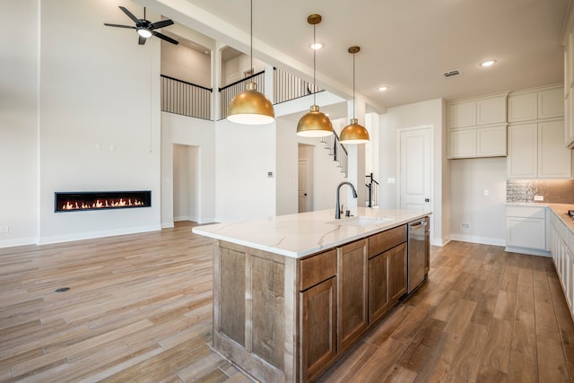 kitchen with light hardwood / wood-style flooring, a center island with sink, light stone countertops, decorative backsplash, and sink