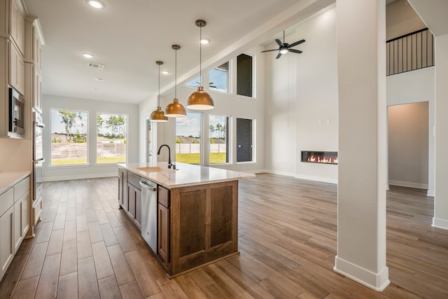 kitchen featuring light hardwood / wood-style flooring, a kitchen island with sink, appliances with stainless steel finishes, pendant lighting, and a towering ceiling