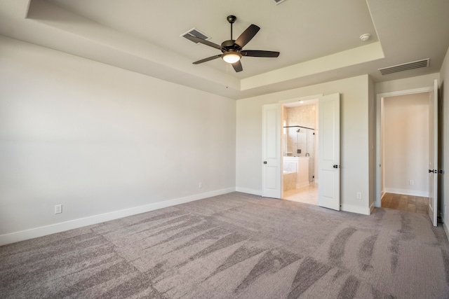 unfurnished bedroom with ensuite bath, ceiling fan, light carpet, and a tray ceiling