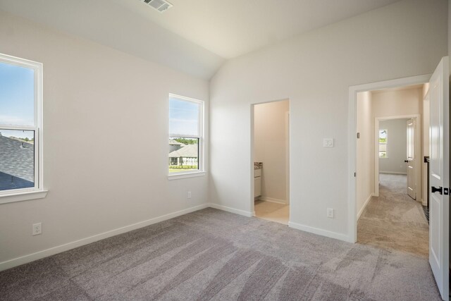 unfurnished bedroom with lofted ceiling, light colored carpet, and ensuite bath