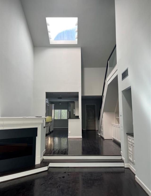 unfurnished living room featuring a towering ceiling and dark wood-type flooring