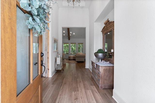 corridor featuring a high ceiling, light hardwood / wood-style flooring, crown molding, and a notable chandelier