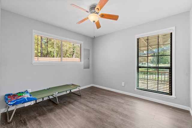 spare room featuring a ceiling fan, electric panel, baseboards, and wood finished floors