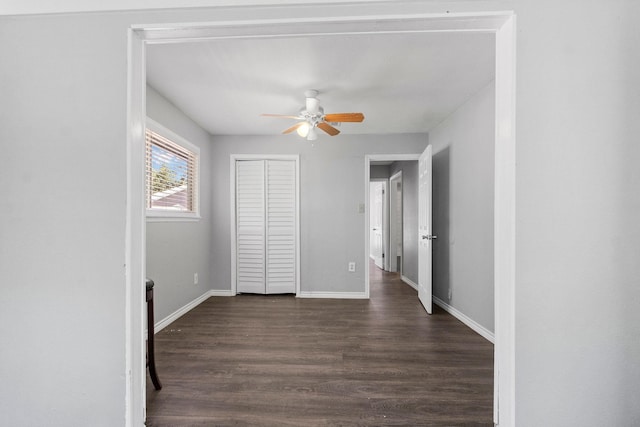 unfurnished bedroom with dark wood-style floors, a closet, ceiling fan, and baseboards