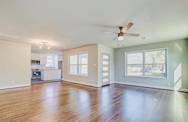 unfurnished living room featuring hardwood / wood-style flooring, a wealth of natural light, sink, and ceiling fan