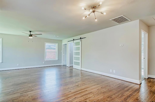 unfurnished room featuring a barn door, ceiling fan with notable chandelier, and light wood-type flooring