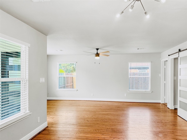 unfurnished living room with ceiling fan, a barn door, and light hardwood / wood-style floors