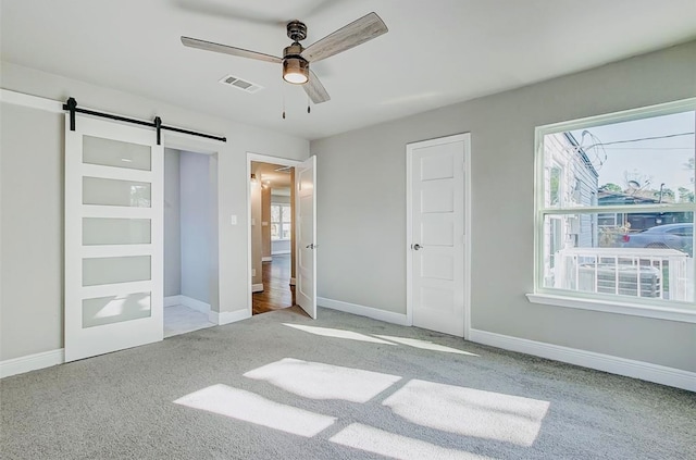 unfurnished bedroom featuring light carpet, ceiling fan, and a barn door