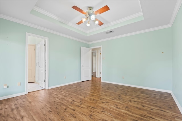 empty room with a tray ceiling, ornamental molding, ceiling fan, and light hardwood / wood-style flooring