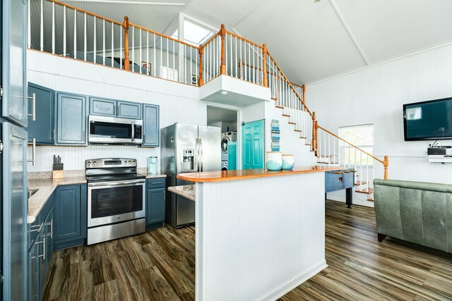 kitchen with dark hardwood / wood-style floors, a high ceiling, stacked washer / dryer, appliances with stainless steel finishes, and blue cabinets