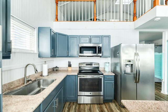 kitchen featuring sink, a high ceiling, dark wood-type flooring, blue cabinetry, and stainless steel appliances