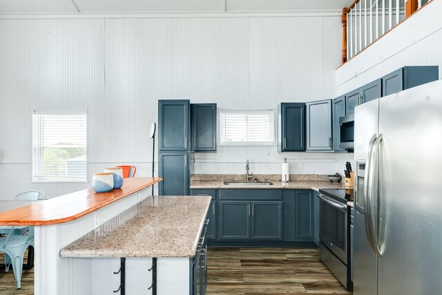 kitchen with dark hardwood / wood-style floors, sink, a high ceiling, appliances with stainless steel finishes, and a breakfast bar area