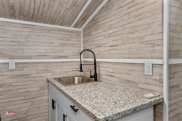 kitchen with sink, light stone counters, white cabinets, vaulted ceiling, and wooden ceiling