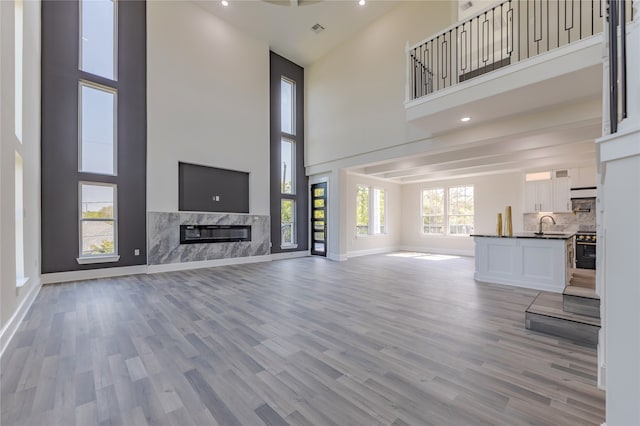 unfurnished living room featuring a fireplace, a high ceiling, sink, and light hardwood / wood-style floors