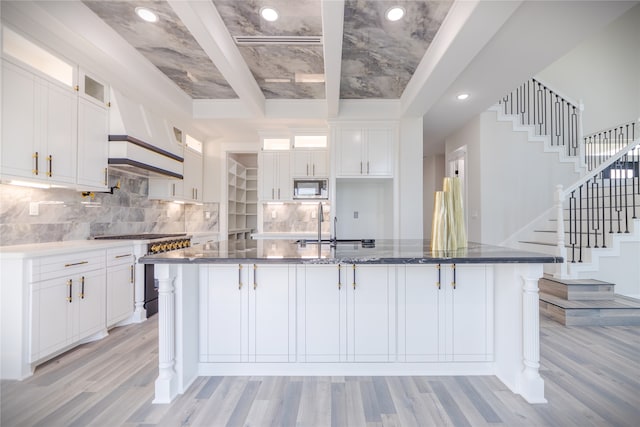 kitchen featuring backsplash, custom range hood, stainless steel appliances, and white cabinetry